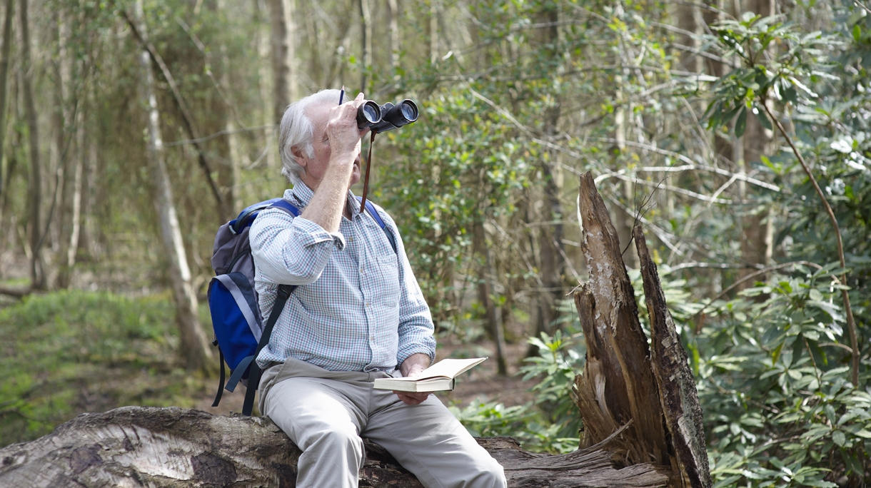 Man looking through binoculars in forest.