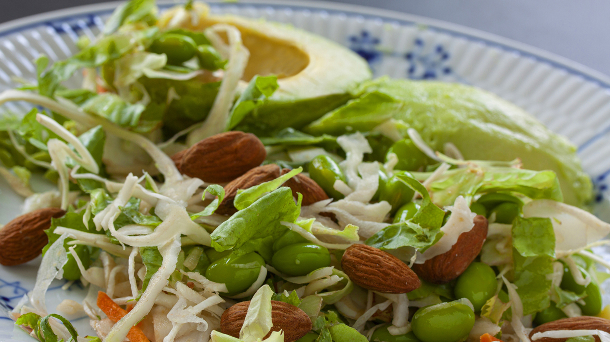 Healthy green raw food organic salad with avocado, edamame beans and almond on a plate.