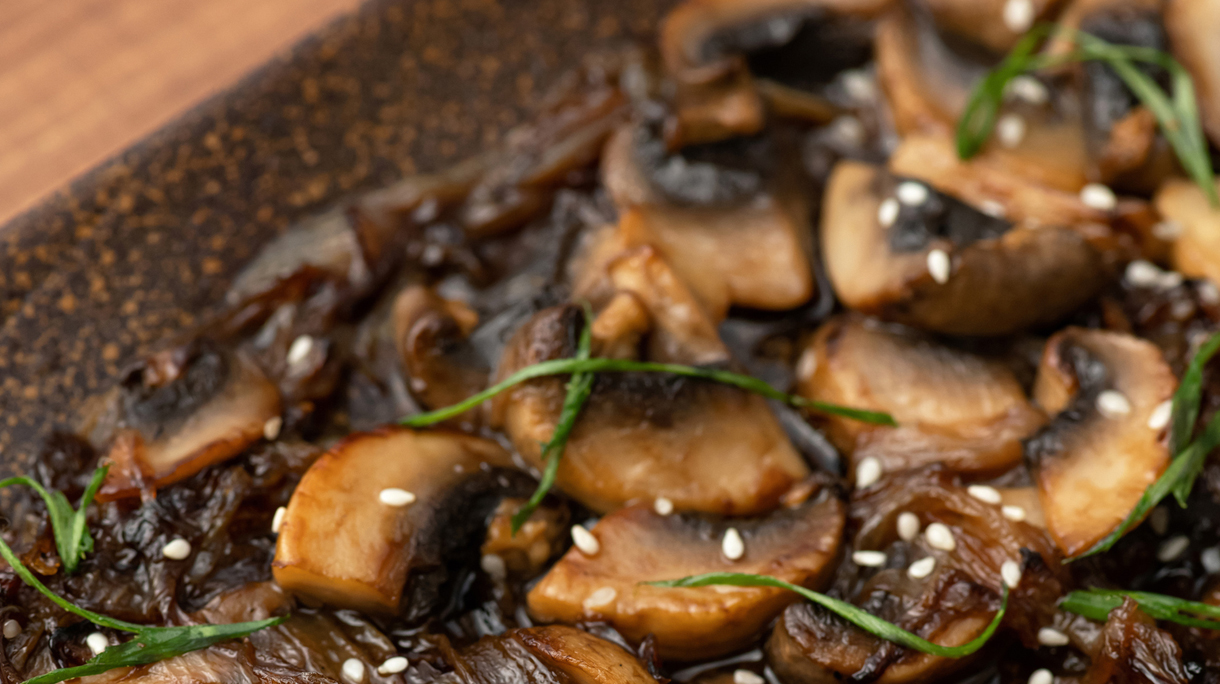Fried mushroom slices on platter. Close-up shot of Clay plate with cooked champignons, herbs and sesame seeds. Soft focus