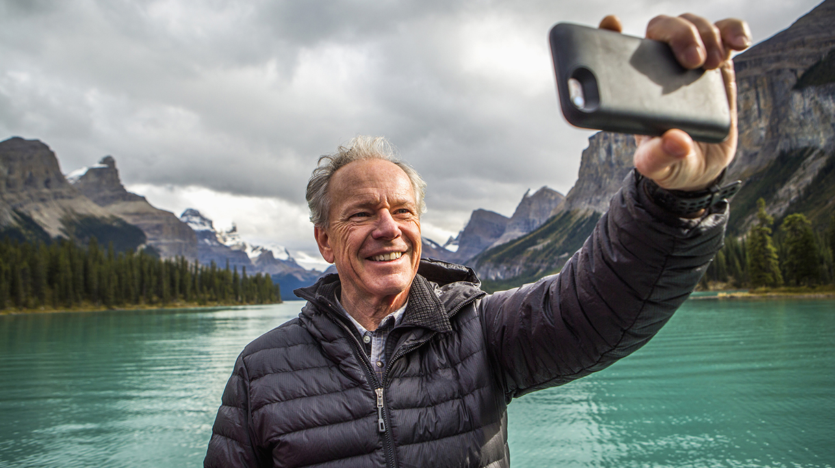 Caucasian man posing for cell phone selfie near mountain lake