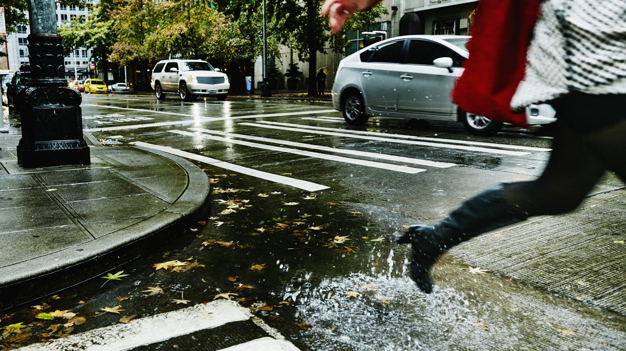 Businesswoman jumping over puddle on city street
