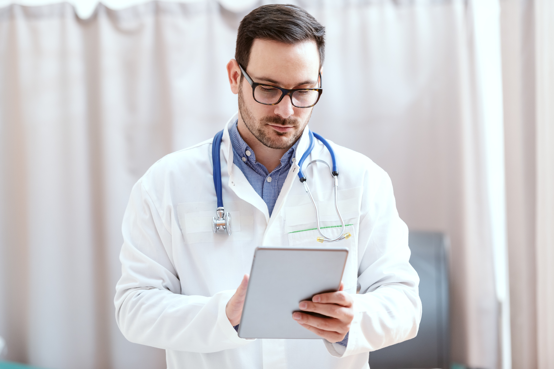 Portrait of Caucasian doctor in uniform and stethoscope around neck using tablet. New technologies in medicine.