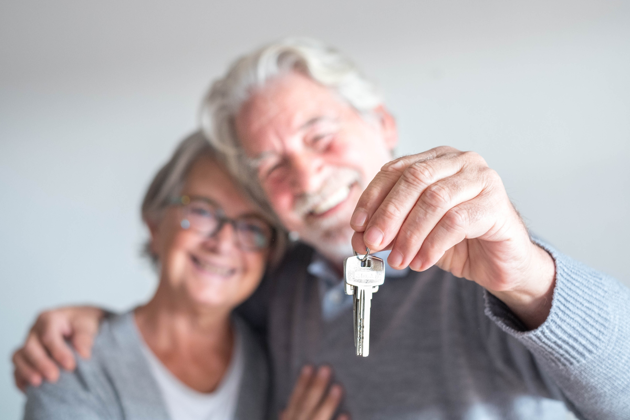 couple of two seniors after buy a new house or car and go to live together – man holding a key and mature man and woman looking at it