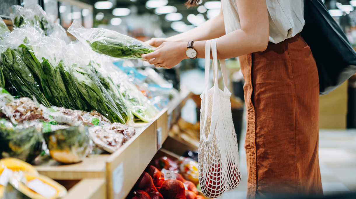 Cropped shot of young Asian woman shopping for fresh organic groceries in supermarket. She is shopping with a cotton mesh eco bag and carries a variety of fruits and vegetables. Zero waste concept