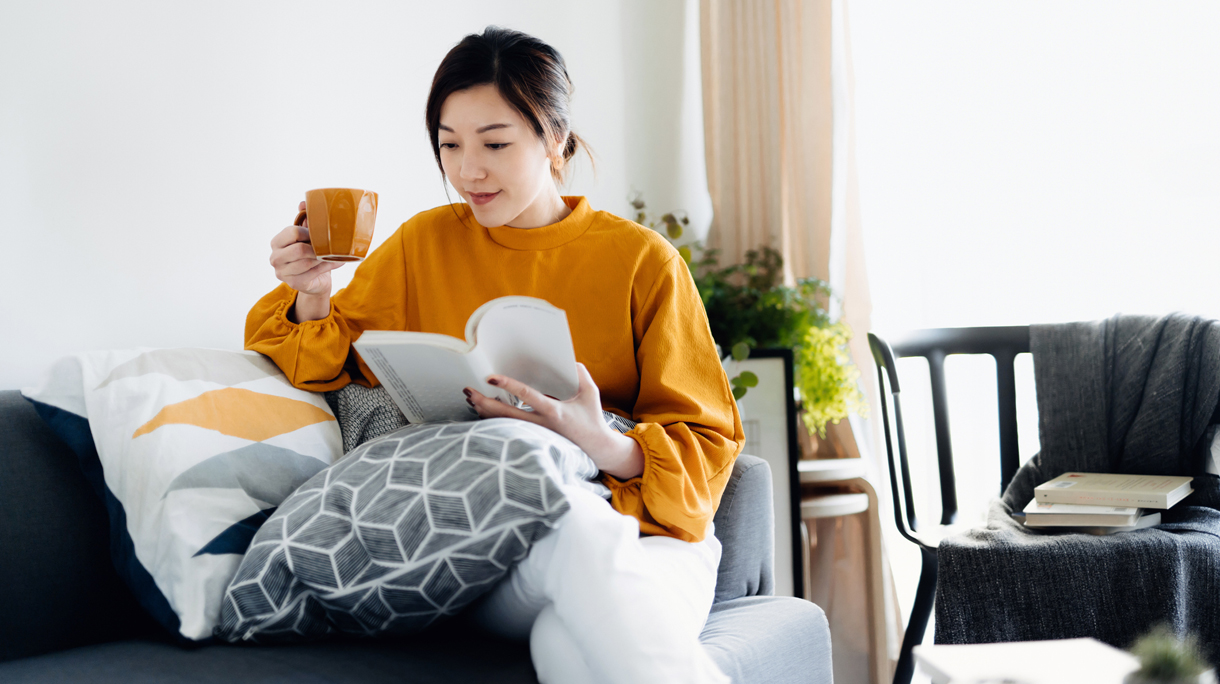 Beautiful young Asian woman reading a book while drinking a cup of coffee. Enjoying a quiet time and relaxing environment at cozy home