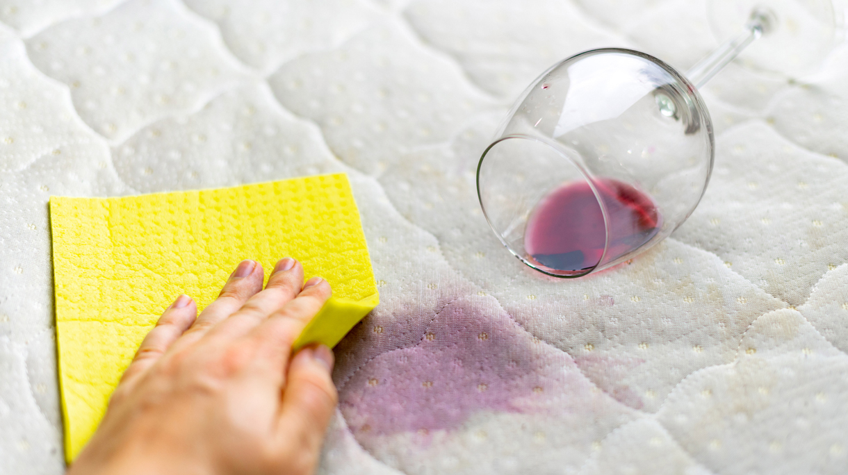 Close-Up Of Woman Hand Wiping Wine Stains From Sofa At Home