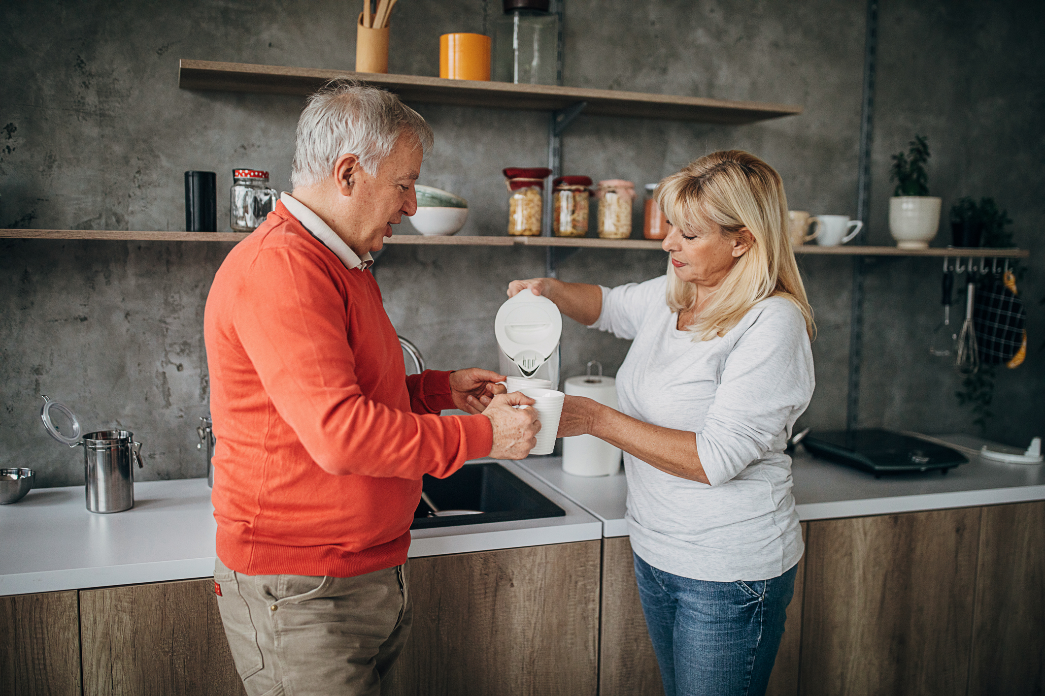 Happy senior couple preparing coffee in kitchen at home
