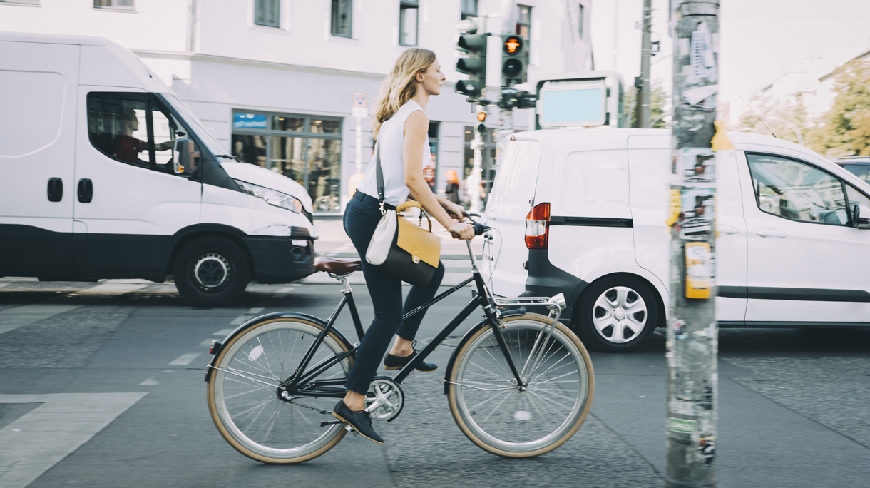 Full length of young businesswoman riding bicycle on road in city