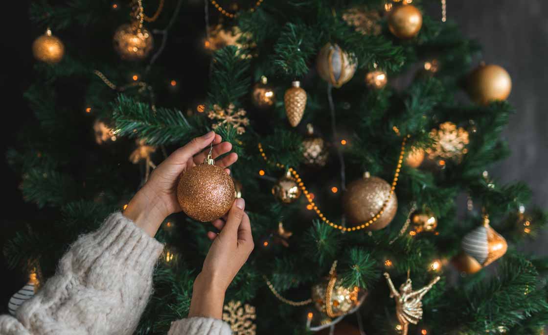 Woman putting on christmas tree golden ornaments.