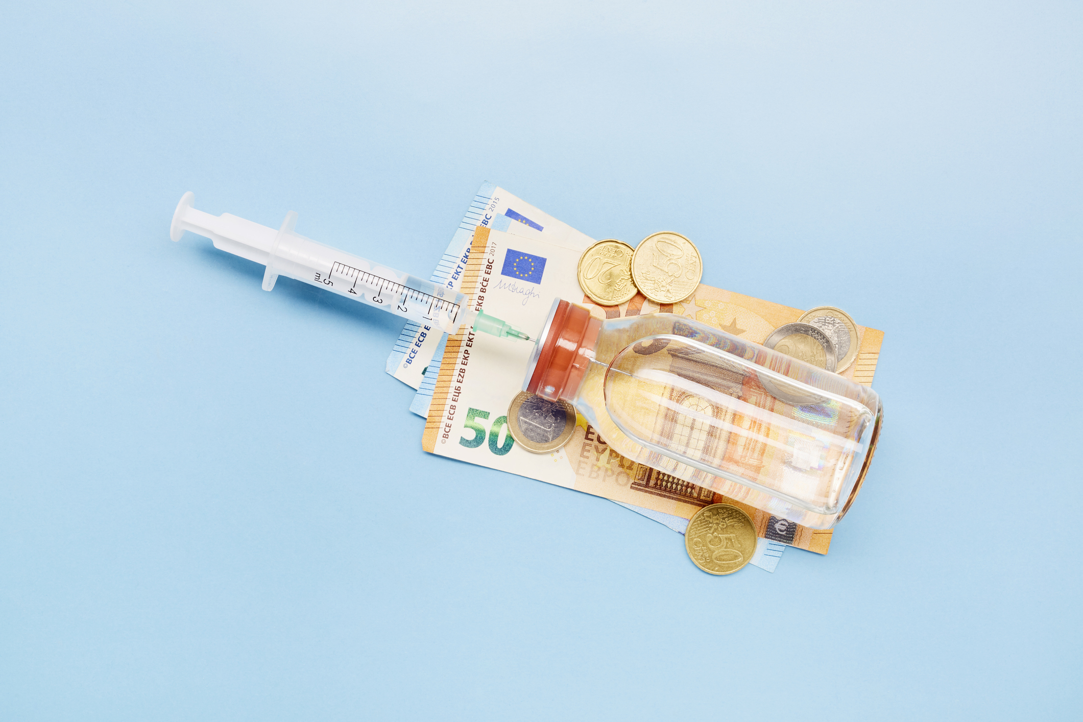 Still life of a syringe, ampoule and Euro banknotes and coins on blue background