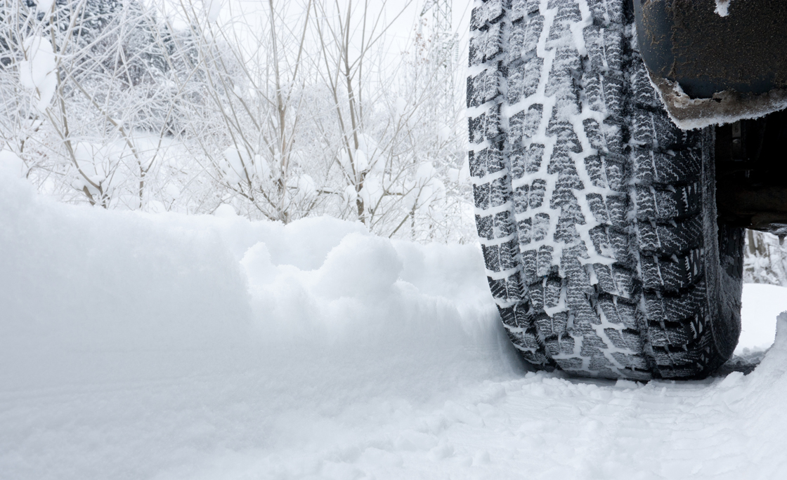 Close-up of a rear black tire in the snow creating tracks