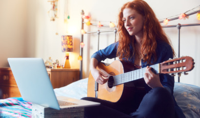 Young woman on bed with guitar and laptop