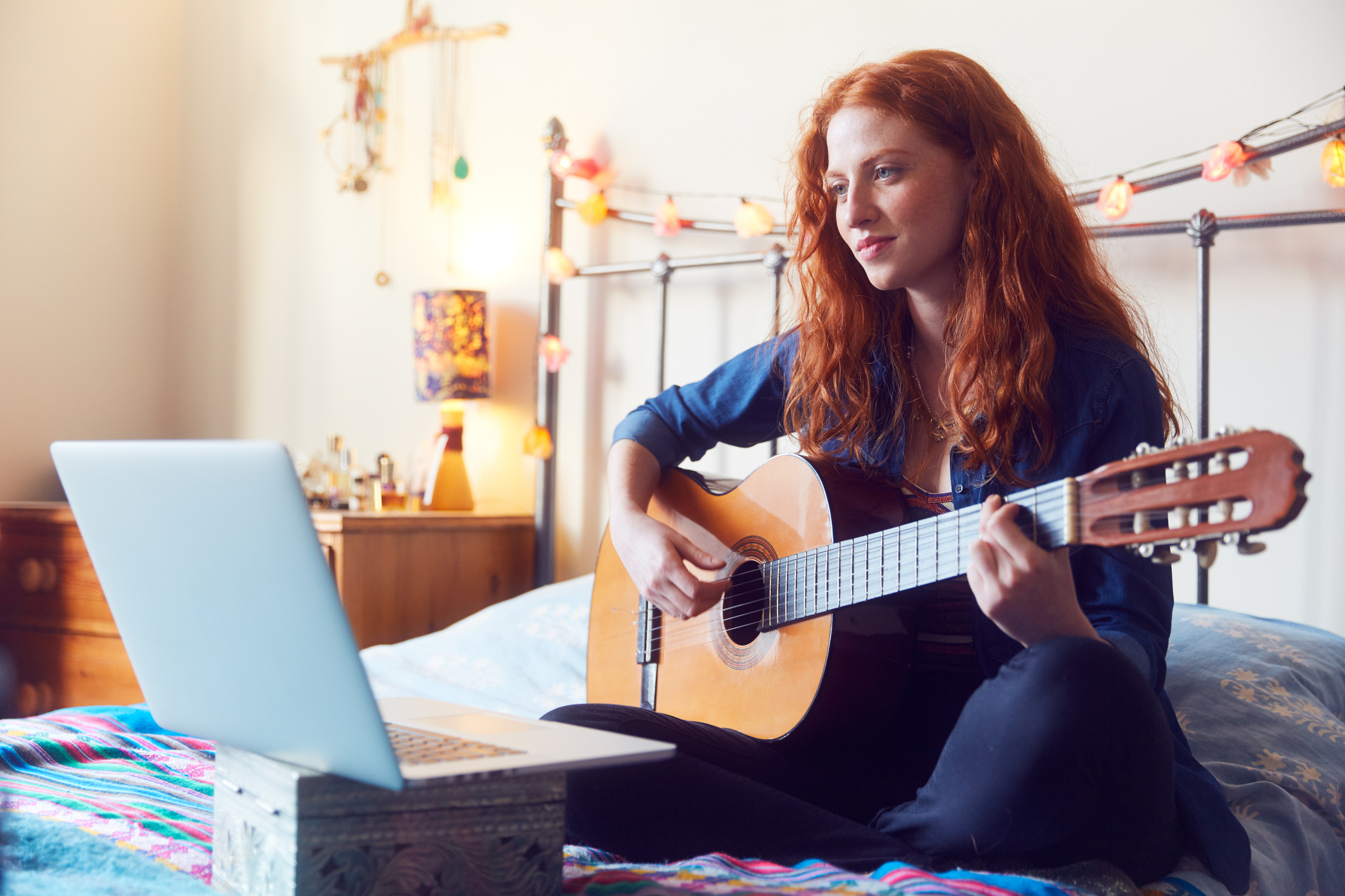 Young woman on bed with guitar and laptop