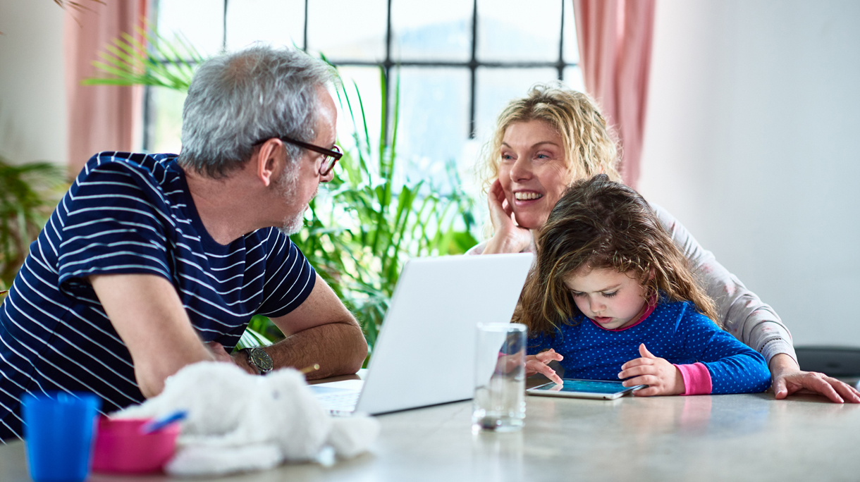 Grandparents looking after granddaughter at home with laptop