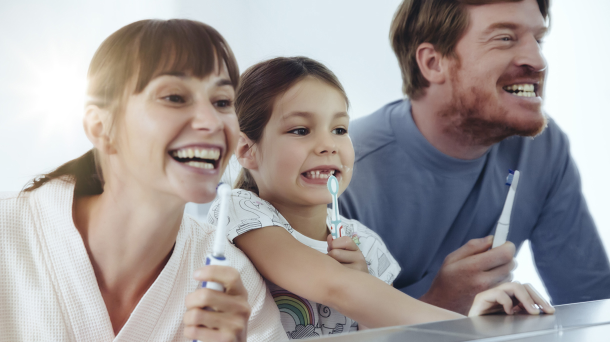 Family of three brushing their teeth in front of big mirror