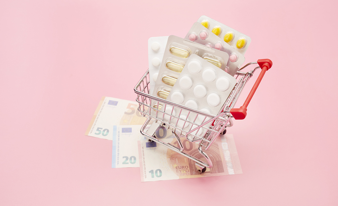 Still life of small shopping cart, pills and Euro banknotes on pink background