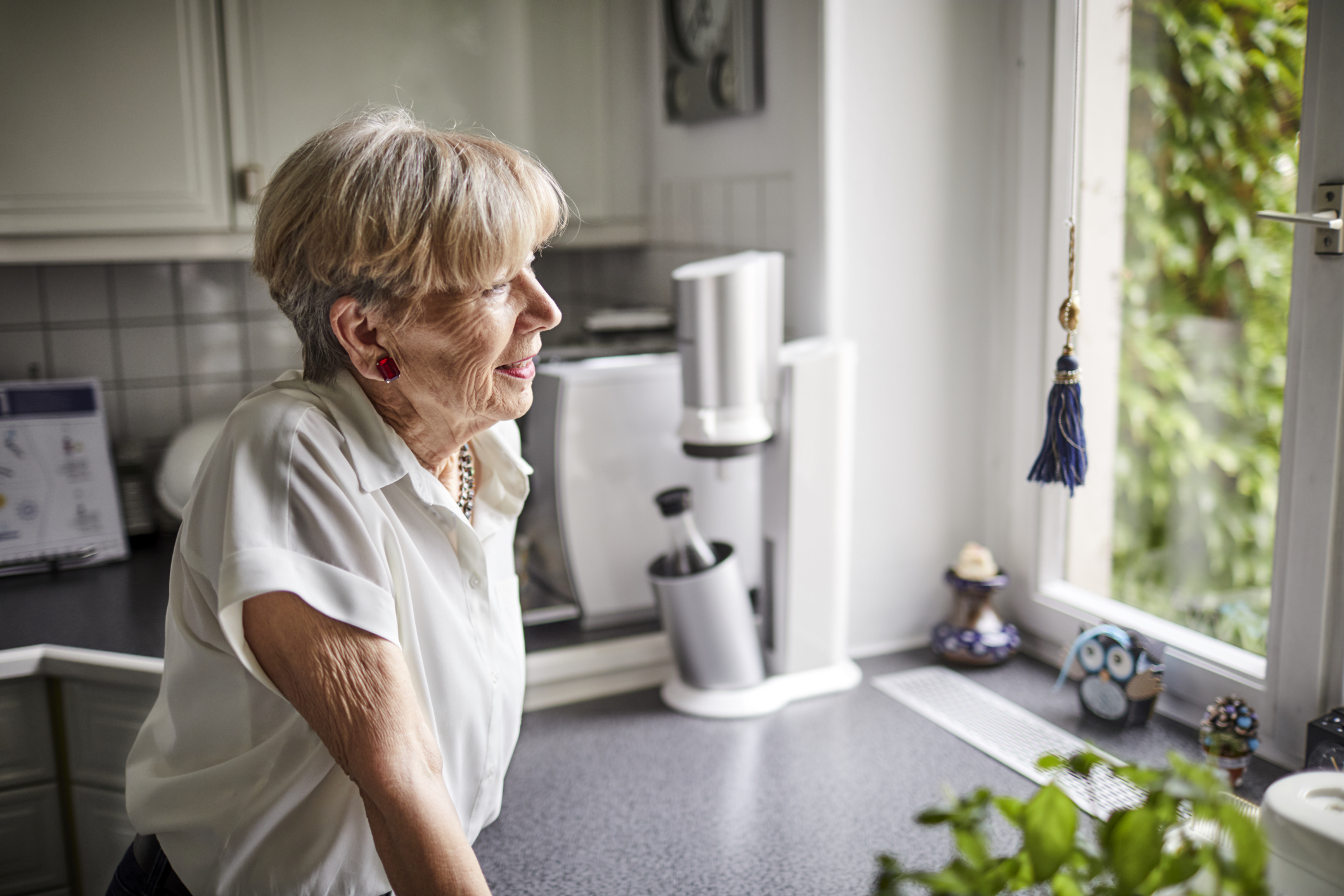 Smiling senior woman in kitchen at home looking out of window