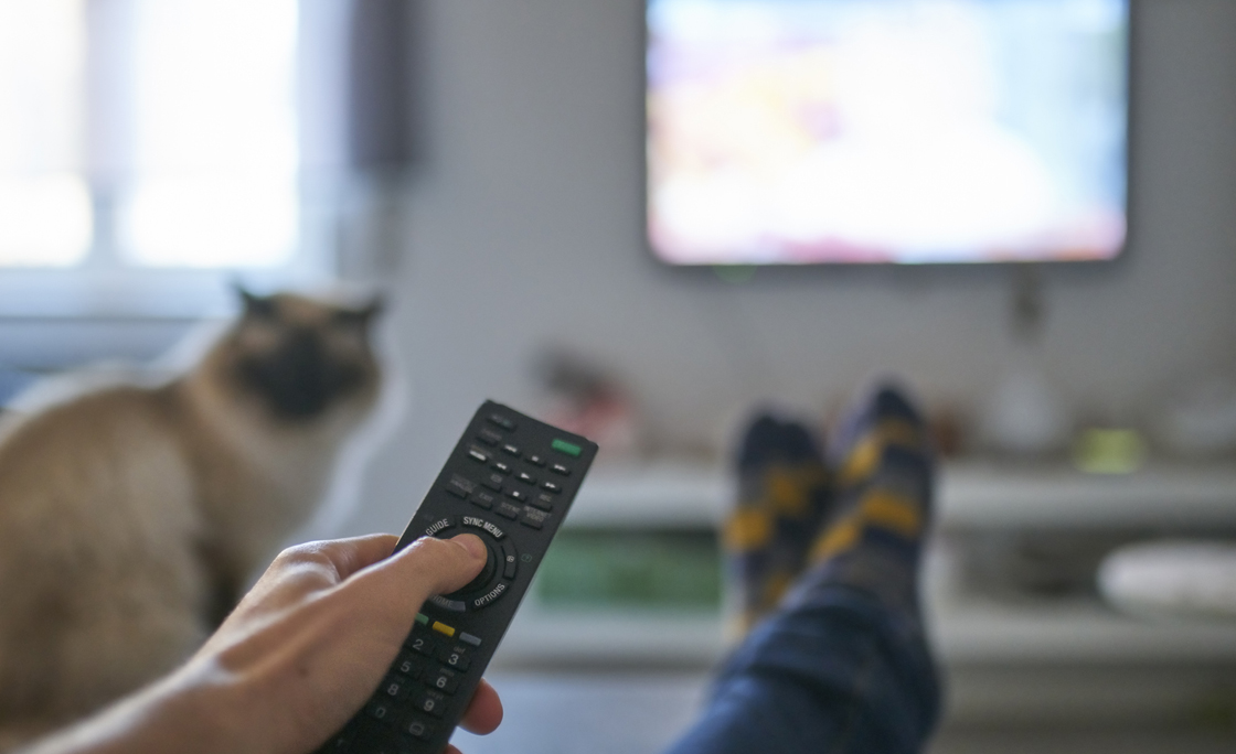 Hand of man pointing remote control at working television screen