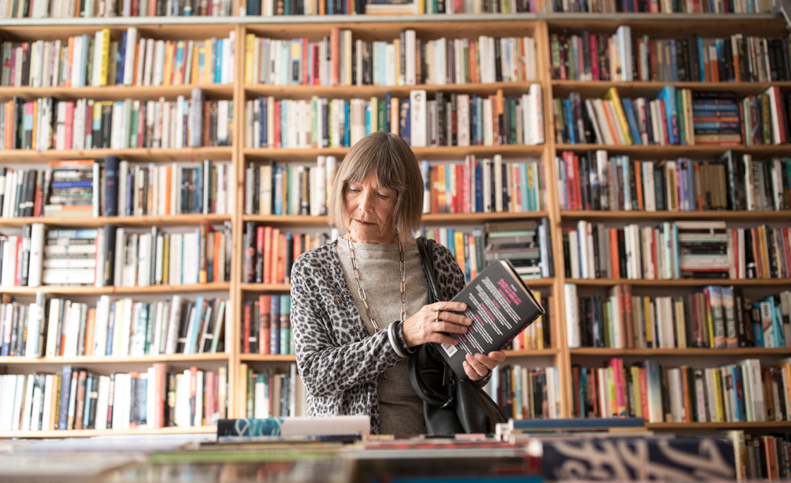 Senior woman with book standing against bookshelf