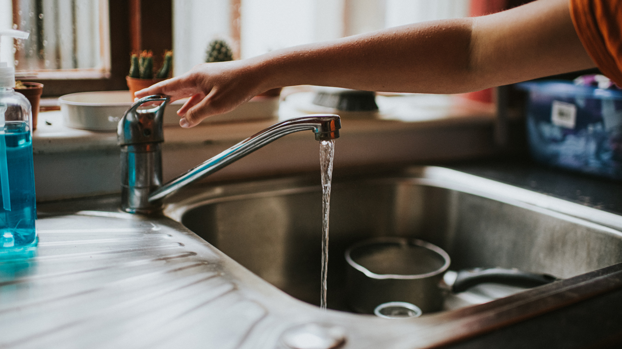 Hand turning off a Running Chrome Tap in a kitchen