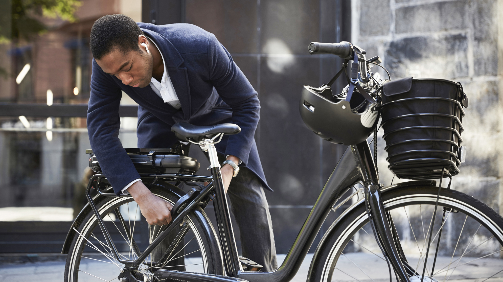 Young male commuter locking electric bicycle against building in city