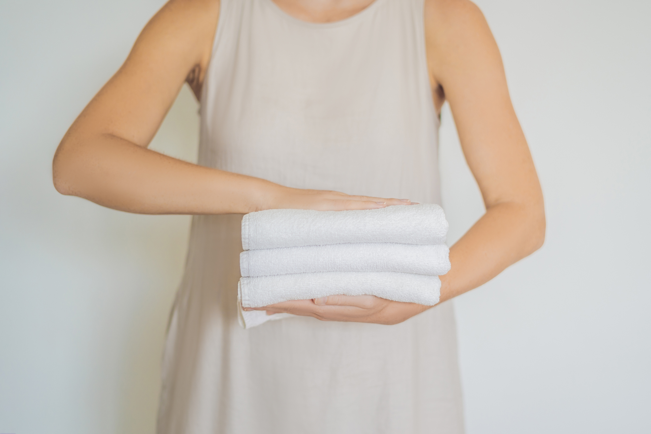 A woman is holding a stack of white towels. Concept of service in hotels, laundry, spa