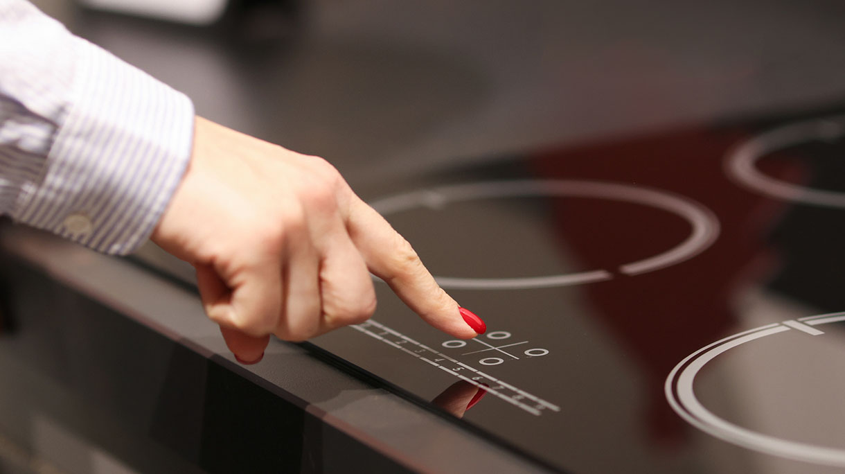 Female finger presses button on touch electric stove