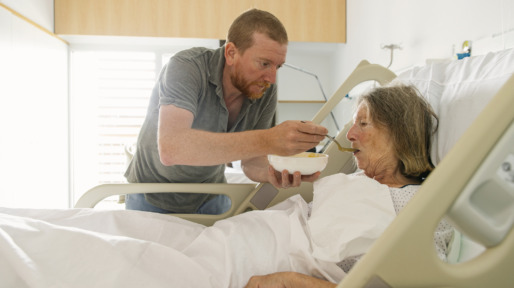 Adult son feeds elderly mother in hospital