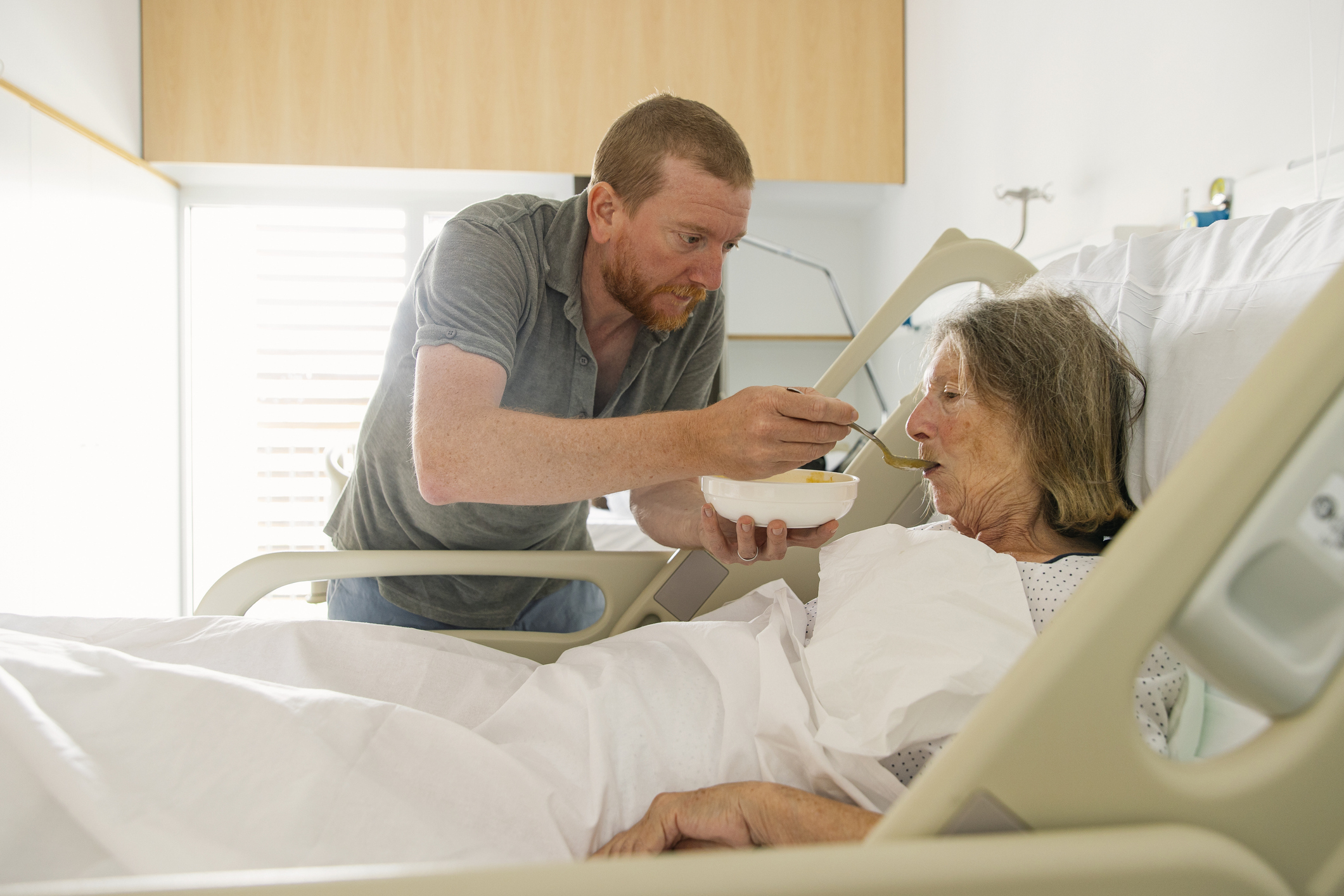 Adult son feeds elderly mother in hospital