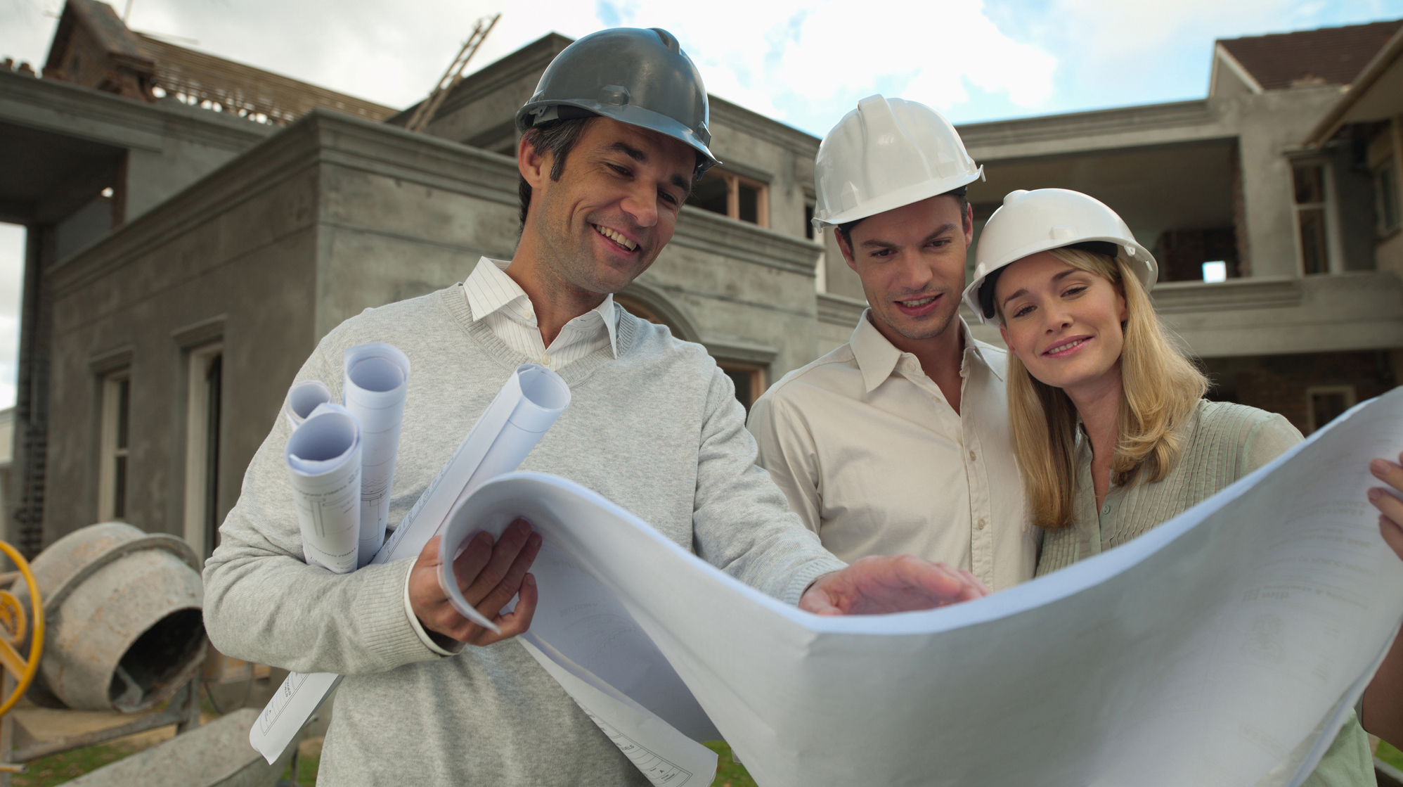 Architect and couple looking at blueprints outside house under construction