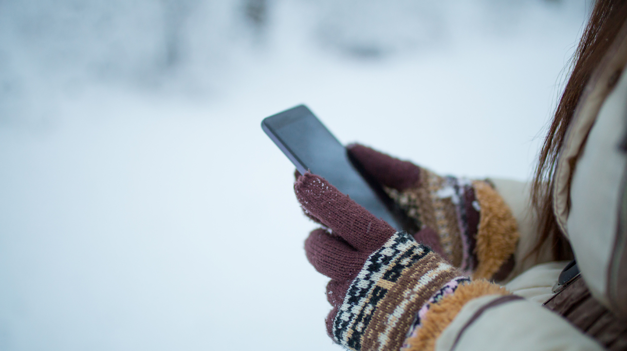 Female hands holding a cellphone outdoors in the snow