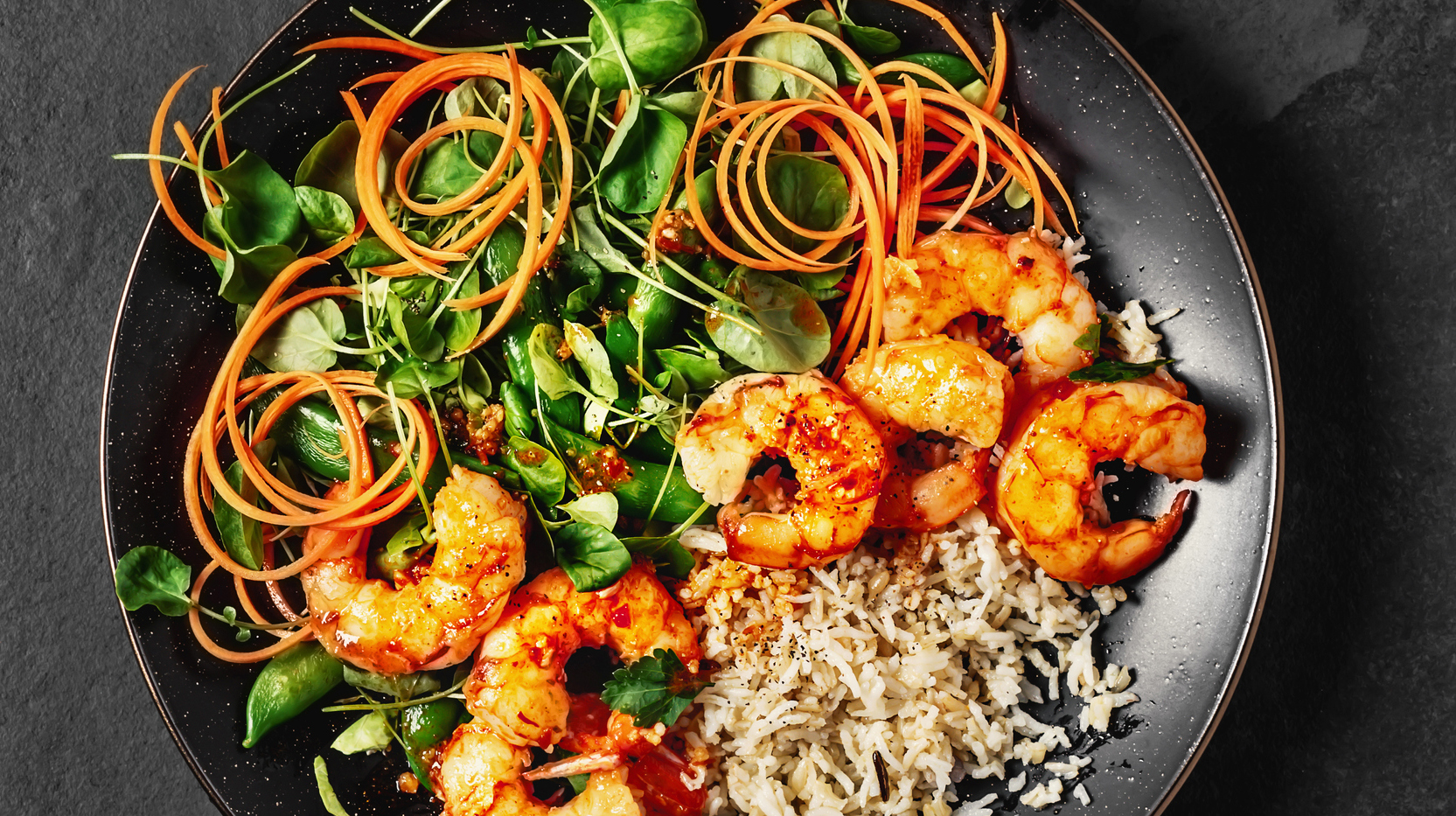 A plate of fresh salad with rice and cooked shrimp on black background