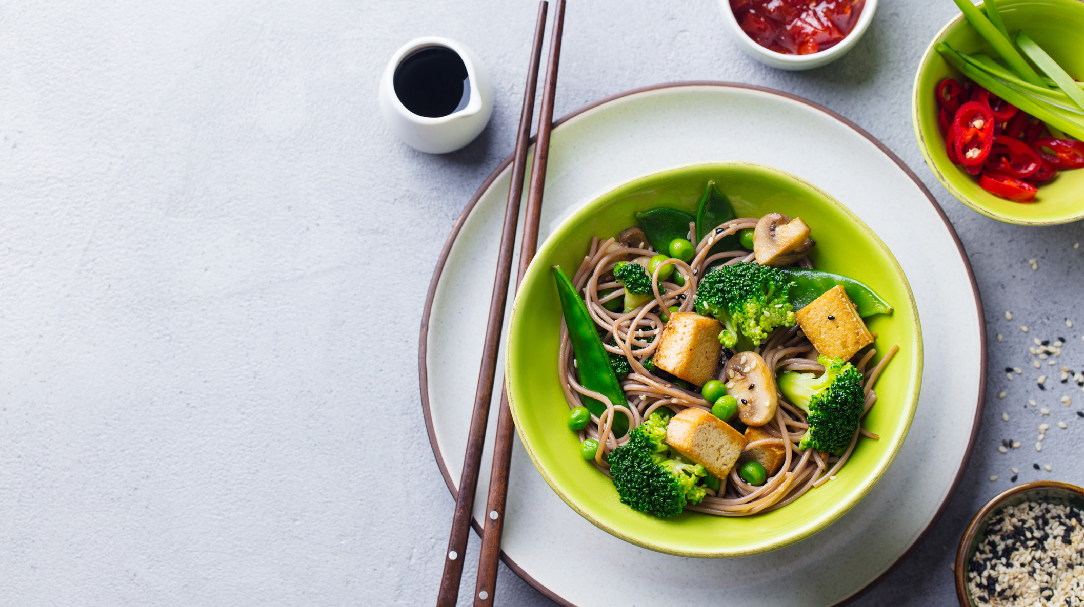 Soba noodles with vegetables and fried tofu in a bowl. Grey background. Copy space. Top view.