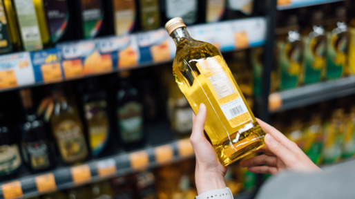 Close up of young woman grocery shopping in a supermarket. Standing by the aisle, holding a bottle of organic cooking oil, reading the nutritional label and checking ingredients at the back