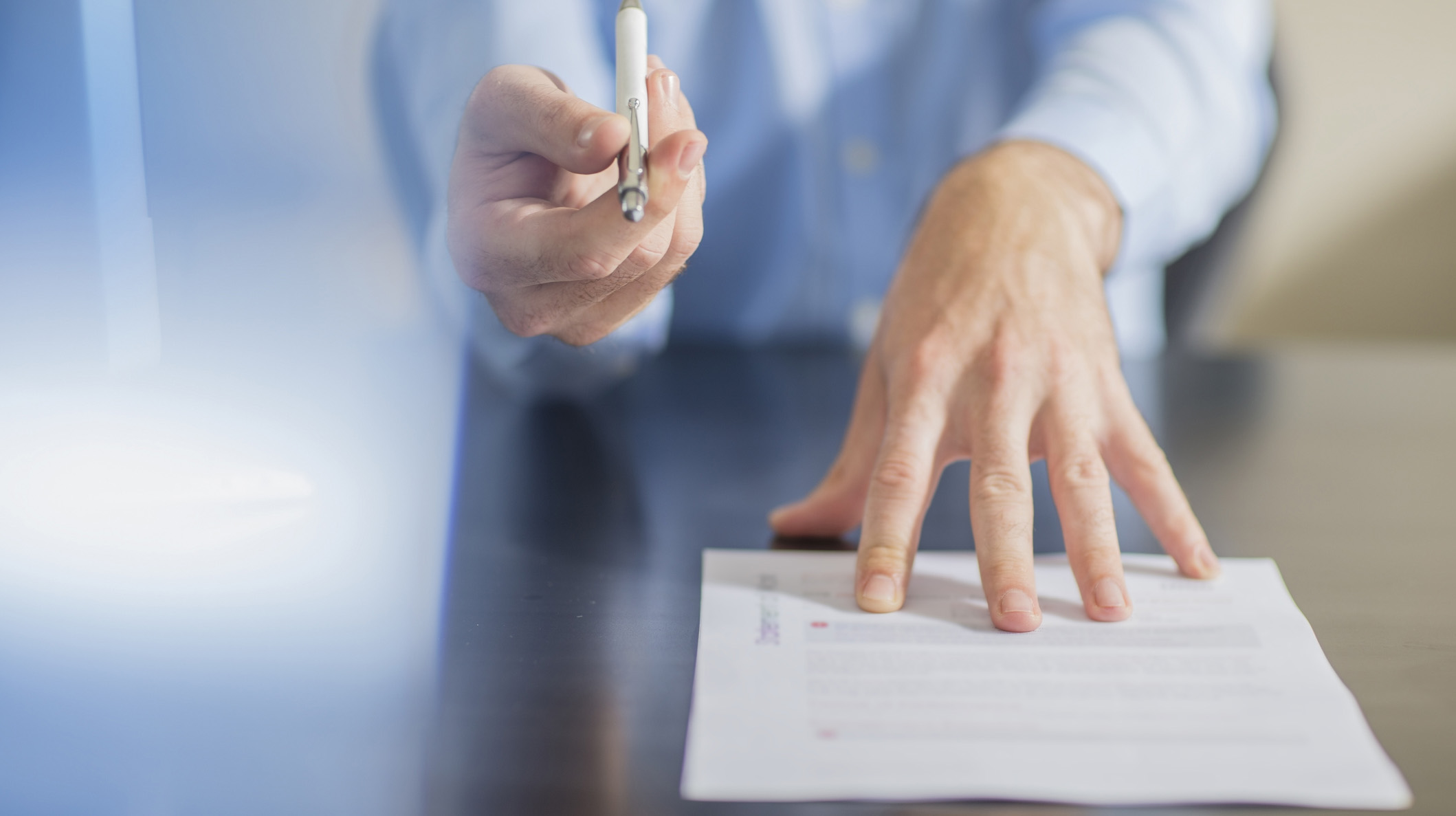 Person sitting at office desk presenting ballpen and contract