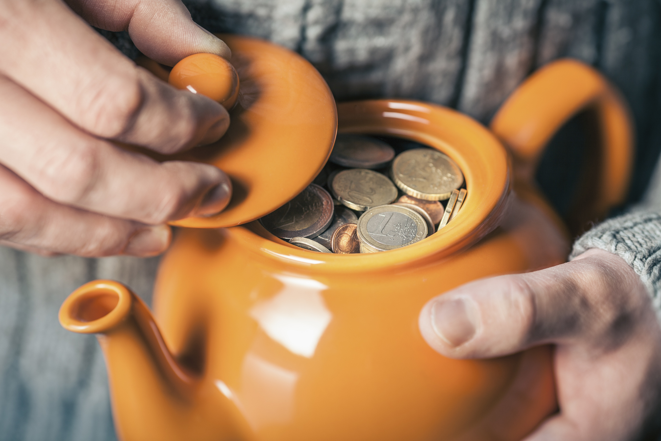 Close up of mans hands holding teapot full of coins