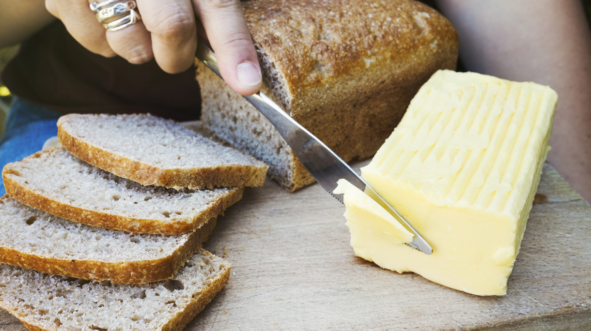 A person with a knife slicing through a block of butter for a sliced bread loaf.