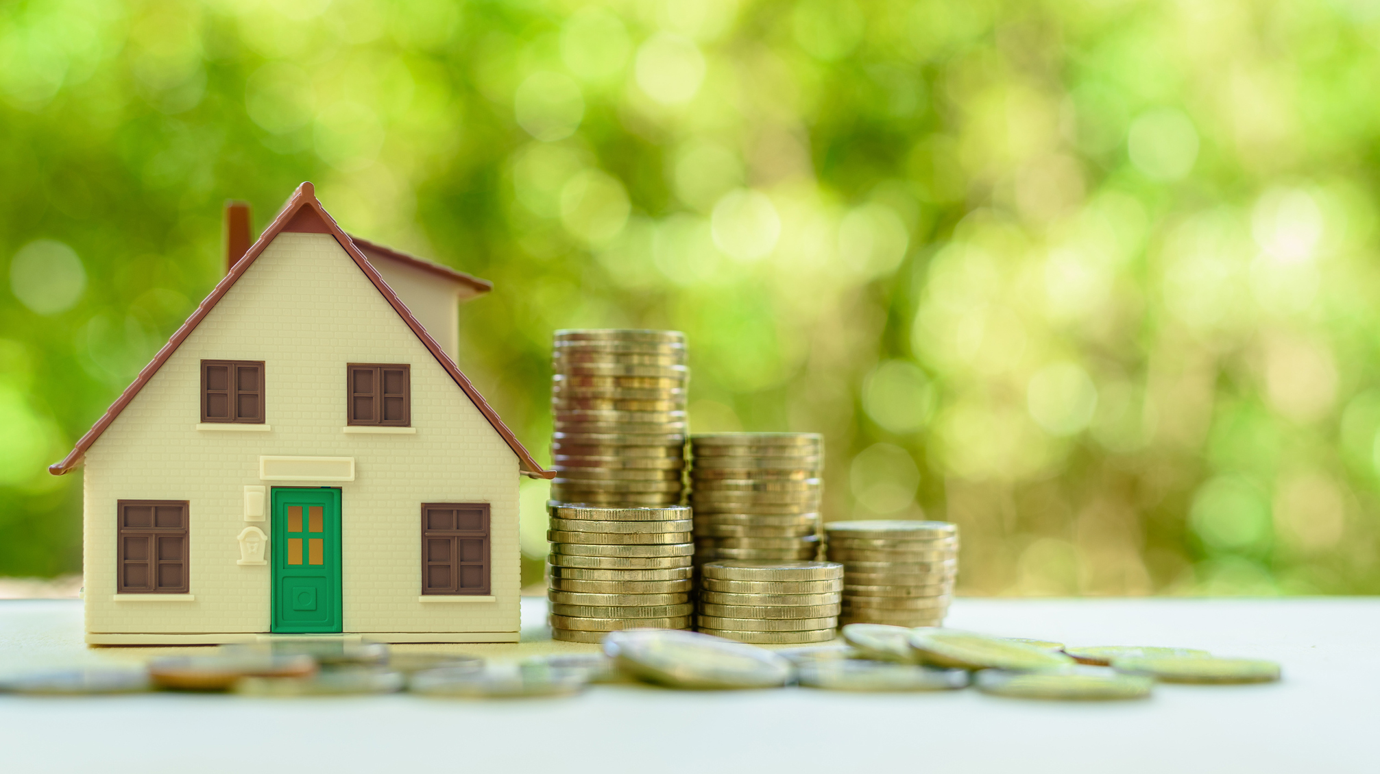 Property investment / reverse mortgage, financial concept : Small home or house model with green door and stacks of rising coins, depicts saving money to buy a new residential asset, human basic needs