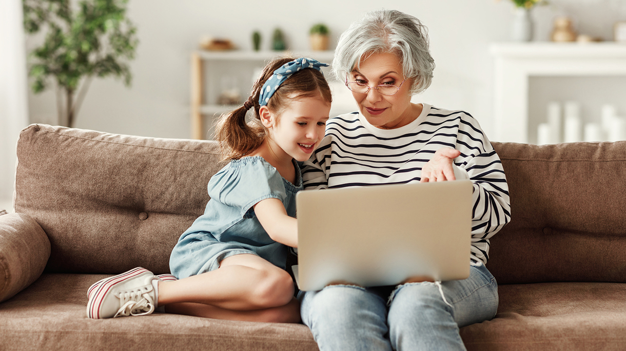 Little child girl with grandmother using laptop at home