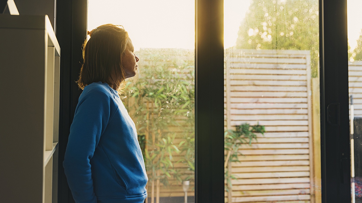 Woman looking out of back door at sunset