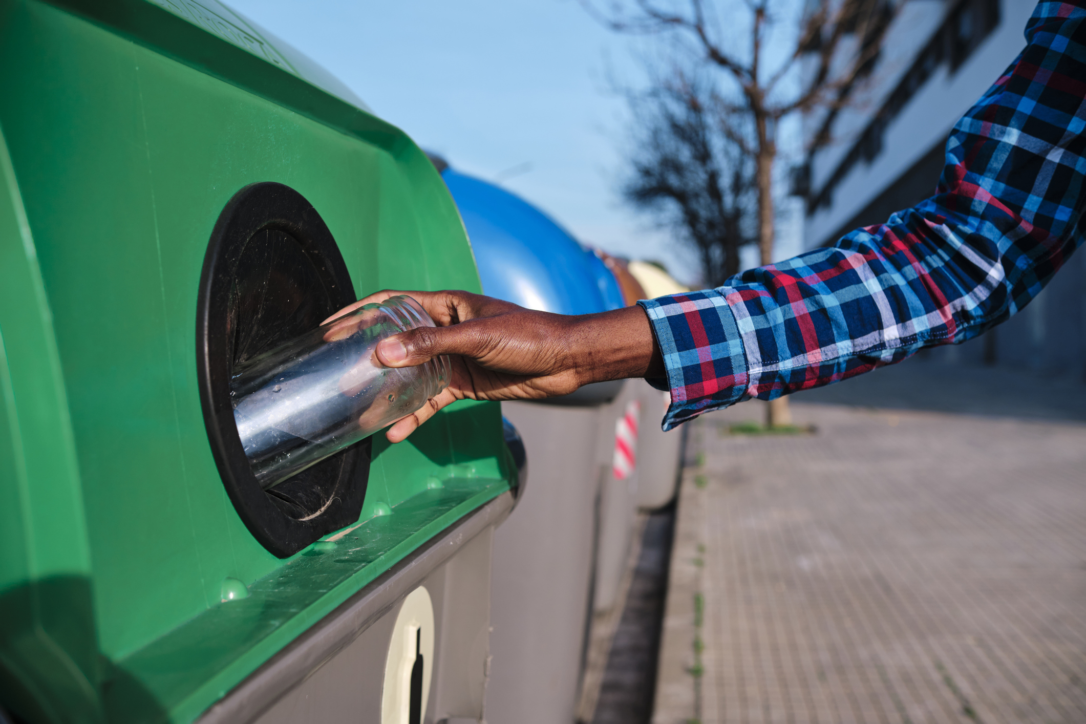 Man putting glass jar in recycling bin on footpath