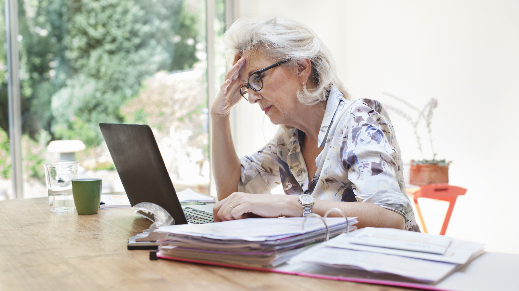 Senior woman sitting at table, using laptop, worried expression
