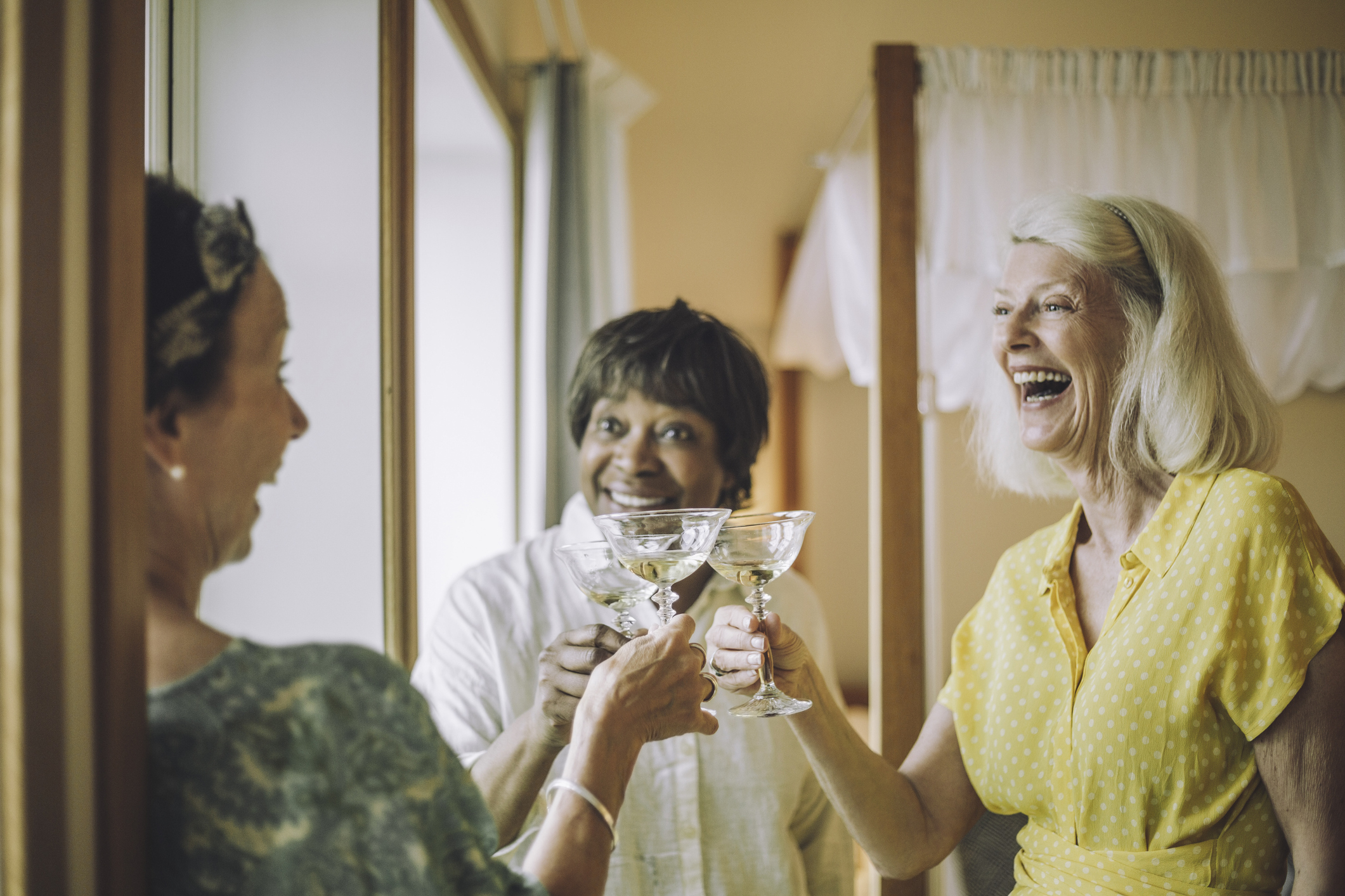 Cheerful senior women toasting champagne glasses in hotel room during vacation
