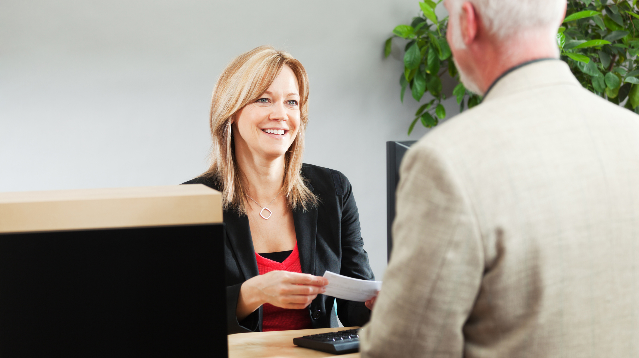 Bank Teller Serving Customer Over Retail Banking Service Counter