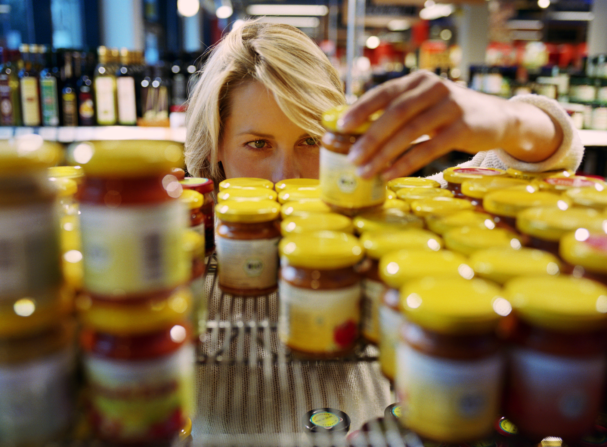 Young woman selecting jar from shelf in shop (focus on woman’s face)