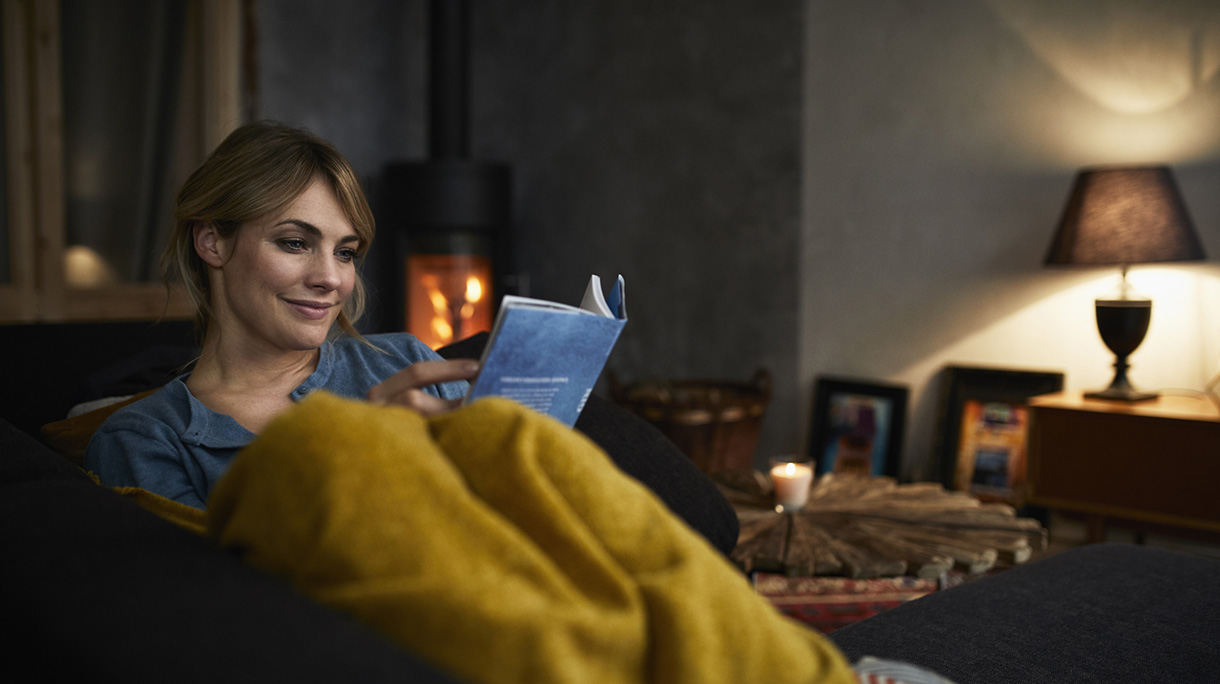 Portrait of smiling woman reading a book on couch at home in the evening