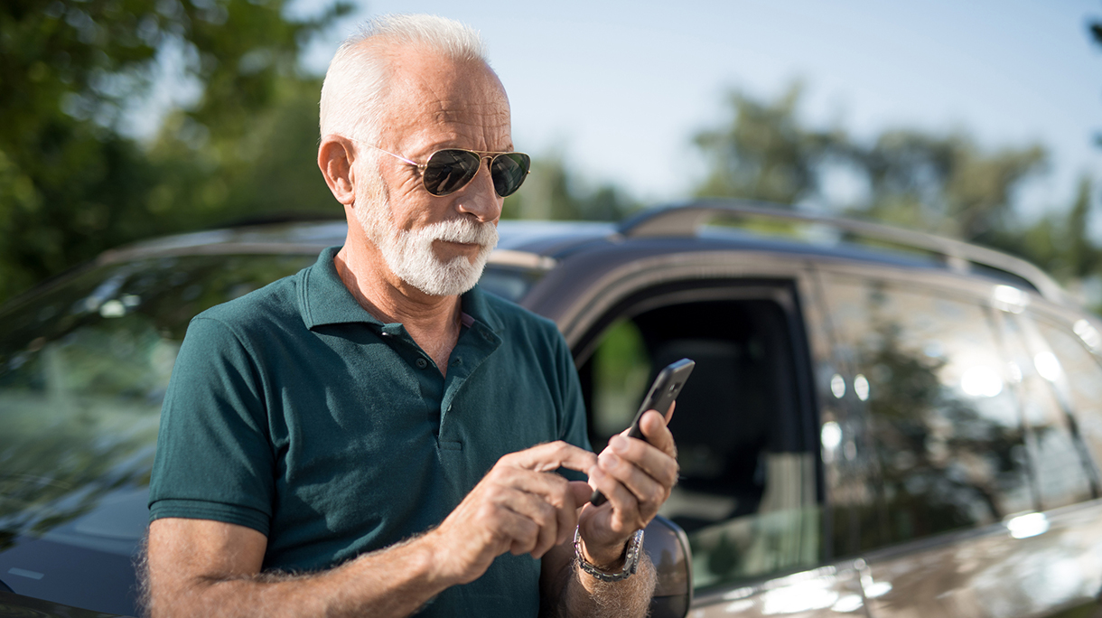Senior man leaning on his car and texting a message.