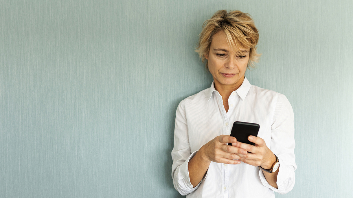 Portrait of mature woman standing at a wall using smartphone