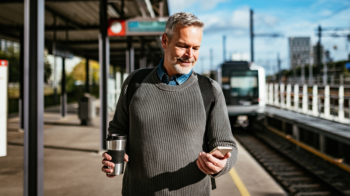 Senior essential worker in city using mobile app on train station