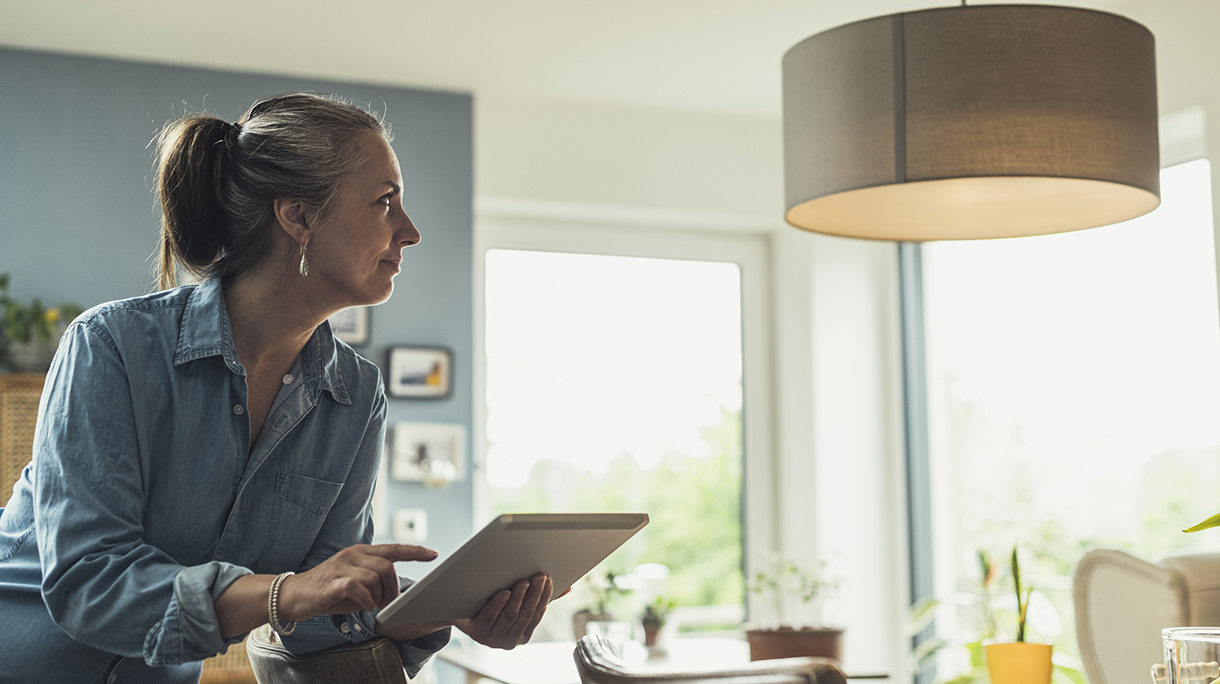Mature woman turning on lighting equipment with digital tablet at home